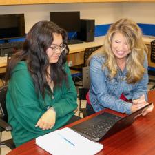 Female Indigenous Support Worker sits with female secondary student working on homework