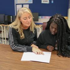 Female Educational Assistant sits with females econdary student working on homework