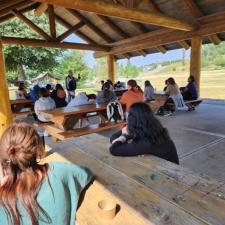 Students sitting at picnic tables listening to an Elder speak