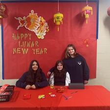 3 Middle school students sitting at a table waiting to hand out coins.